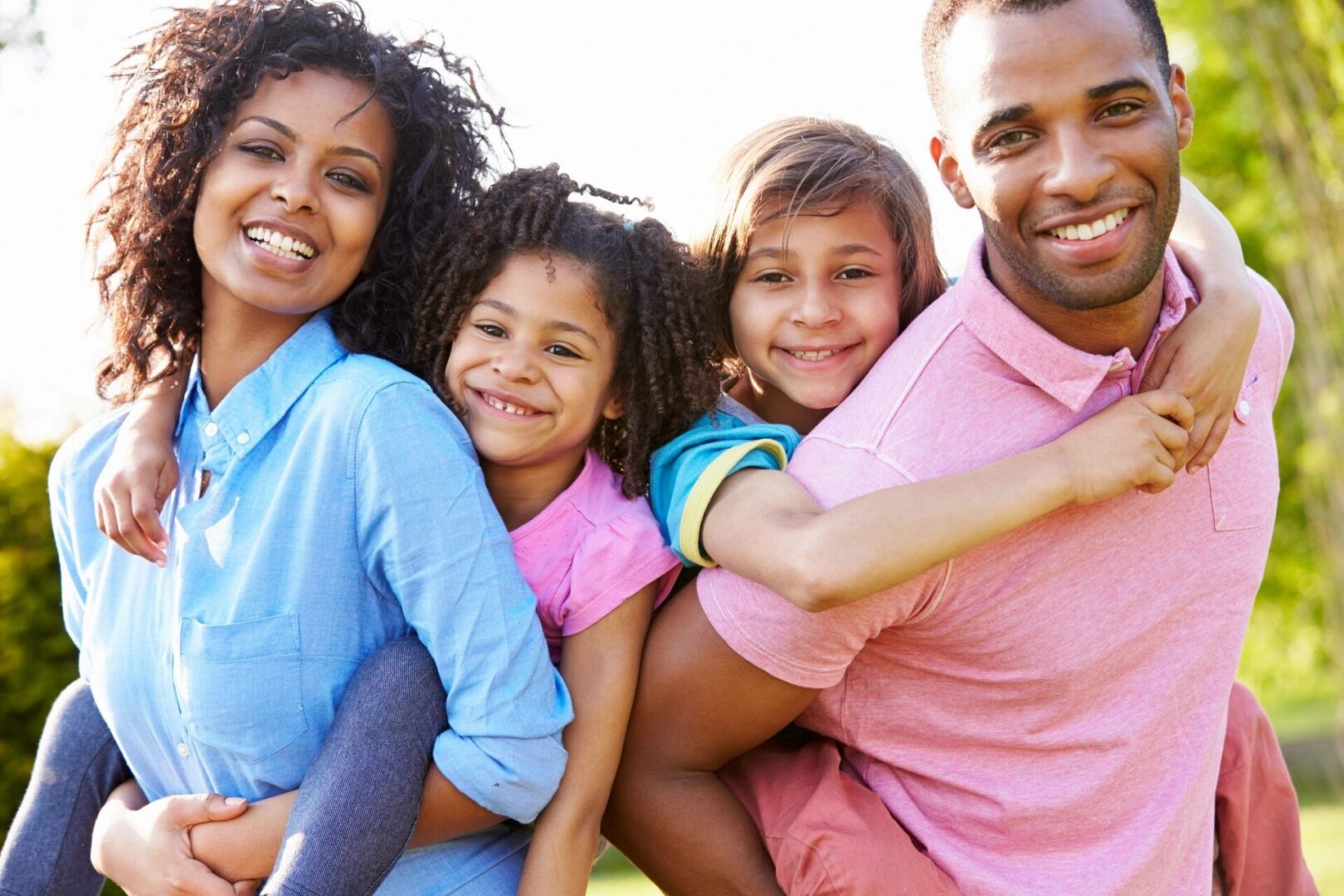 A heterosexual black couple with giving their son and daughter a piggy-back ride