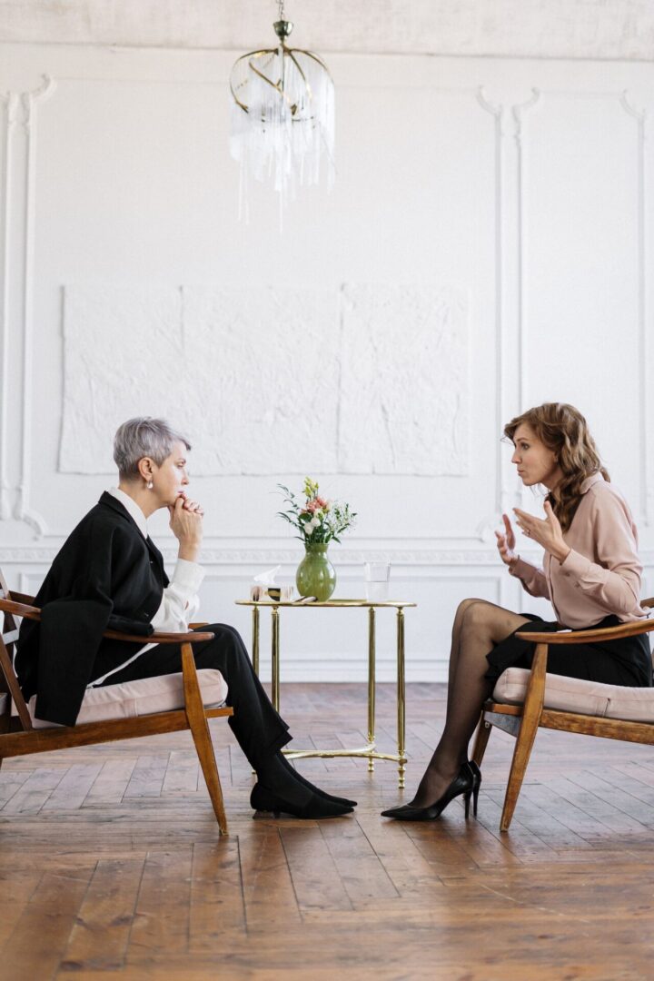 A woman with short white hair listening to a younger woman dressed in business attire